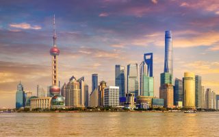 منظرهای از خط افق شانگهای در غروب آفتاب، با آسمانخراشهای برجسته از جمله برج مروارید شرقی، مرکز مالی جهانی شانگهای، و برج شانگهای. آسمان با رنگهایی از صورتی، بنفش و نارنجی رنگآمیزی شده است که از رودخانه Huangpu منعکس میشود—منظرهای به نقاط برجسته رقیب تورهای ترکیبی اروپای کافه سفر.