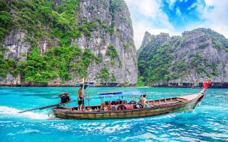 یک قایق سنتی چوبی دم بلند با سایبان آبی بر روی آب‌های فیروزه‌ای شفاف که توسط صخره‌های آهکی سبز و سرسبز در زیر آسمان آبی پر جنب و جوش با چند ابر احاطه شده است حرکت می‌کند. چندین نفر در قایق هستند و در طول تور گروهی پوکت خود از منظره منظره لذت می برند.